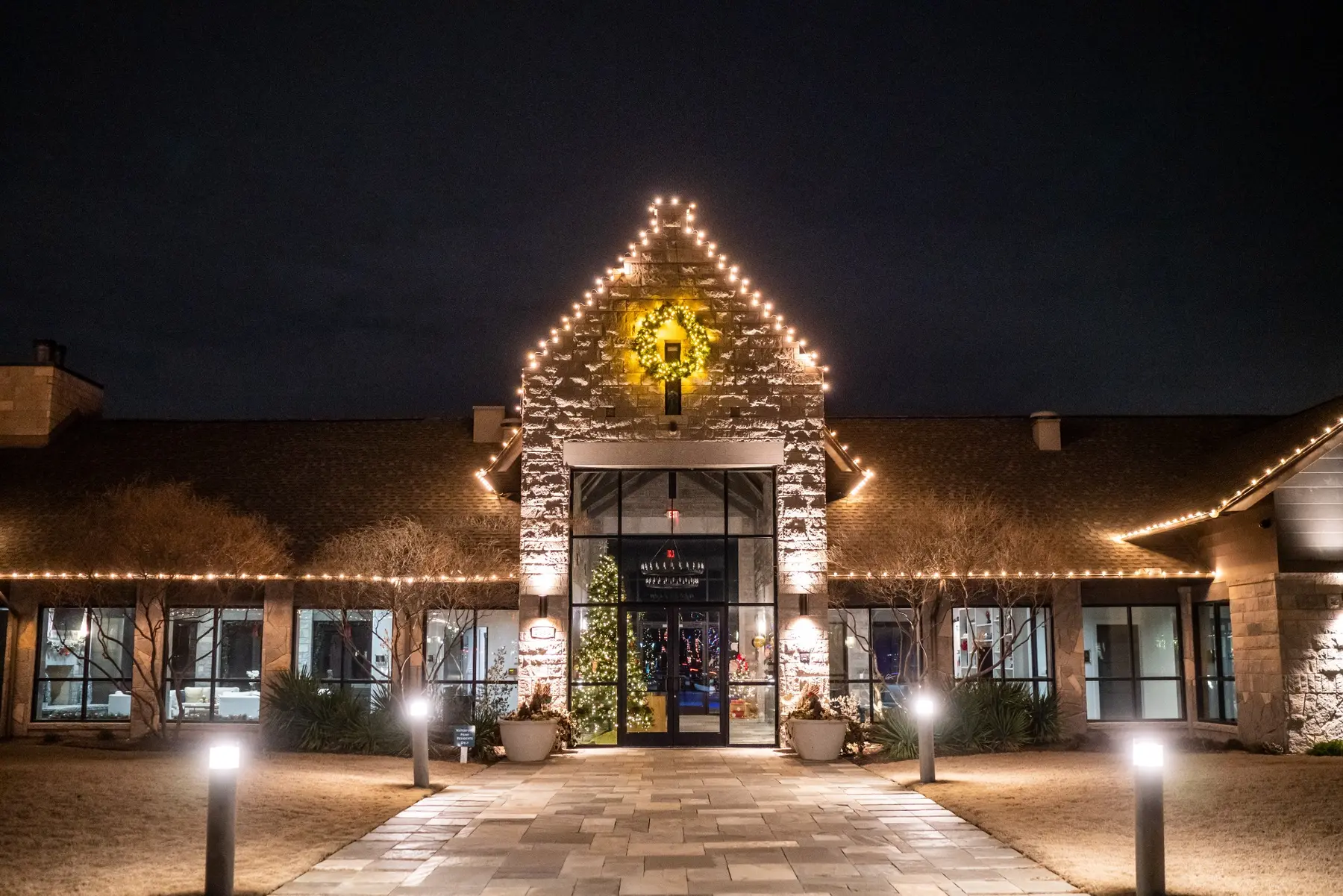 Commercial building outlined with warm white roofline lights and a lit wreath above the entrance