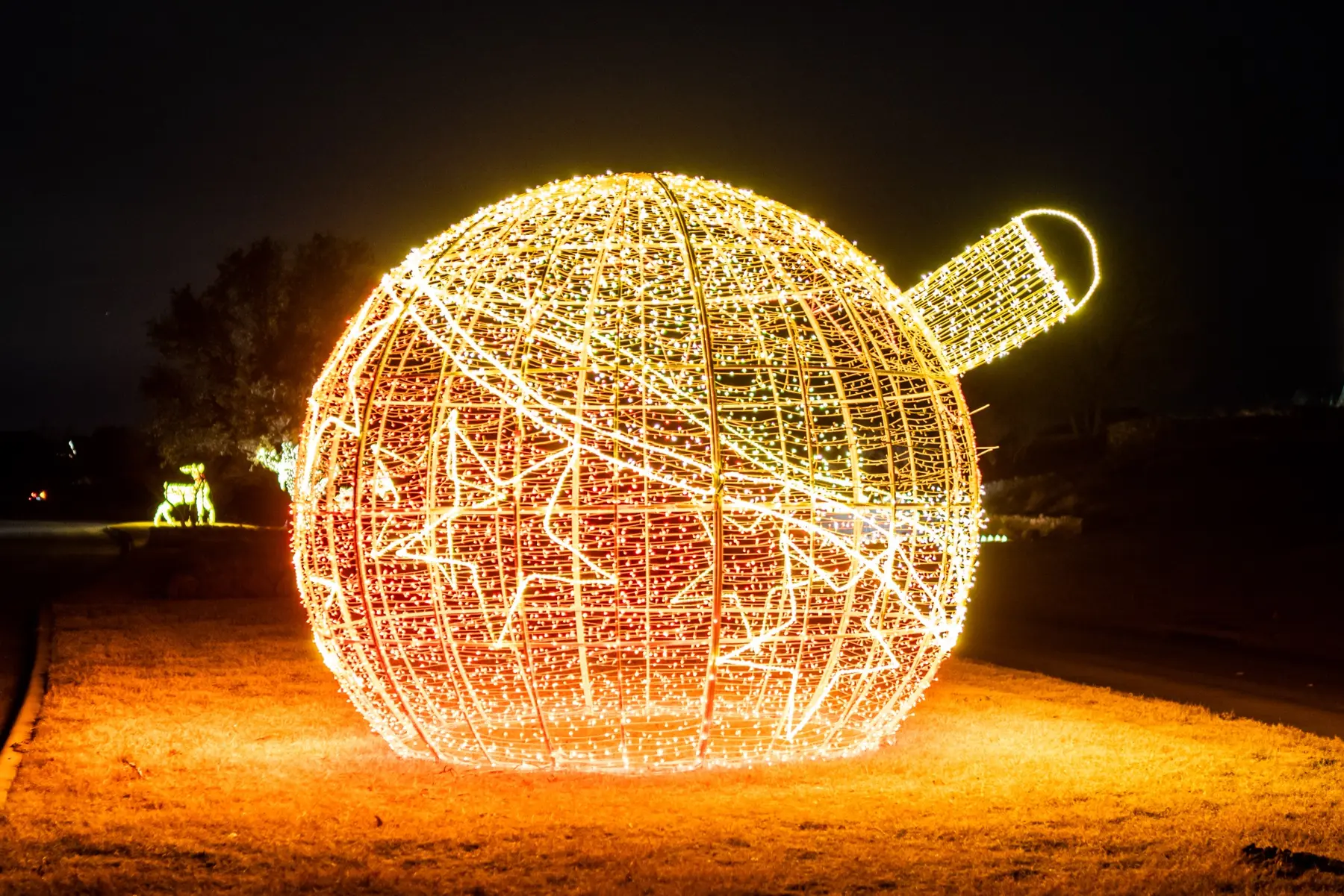 Oversized illuminated Christmas ornament sculpture glowing warm white at night