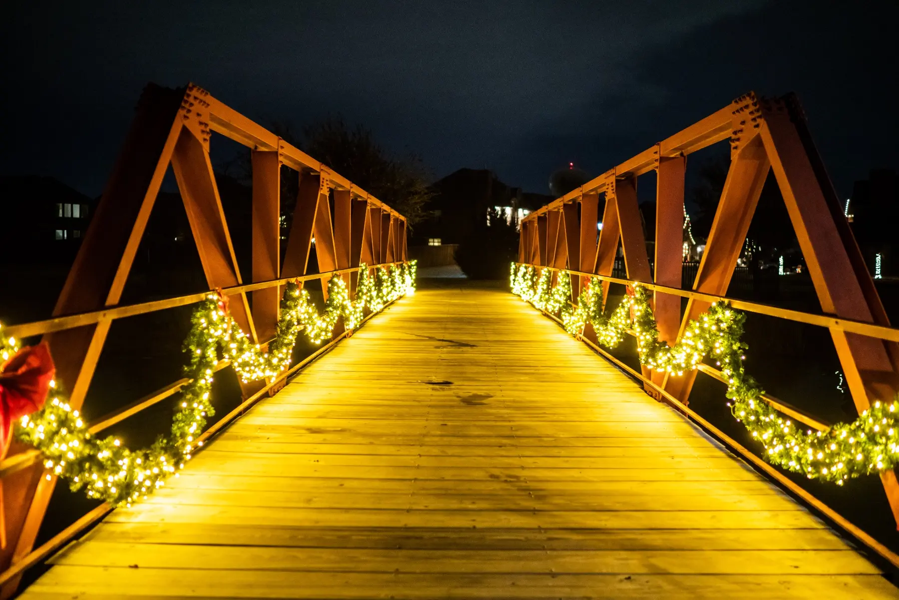 Pedestrian bridge railing draped with lit garland and red bows