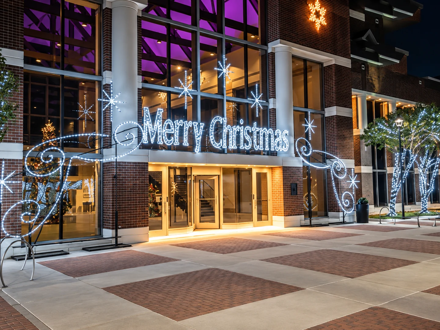 Commercial building entrance with a large illuminated Merry Christmas sign and white-lit trees