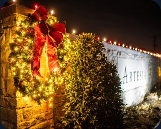 Large holiday wreath with red bow and lit greenery at a community monument entrance