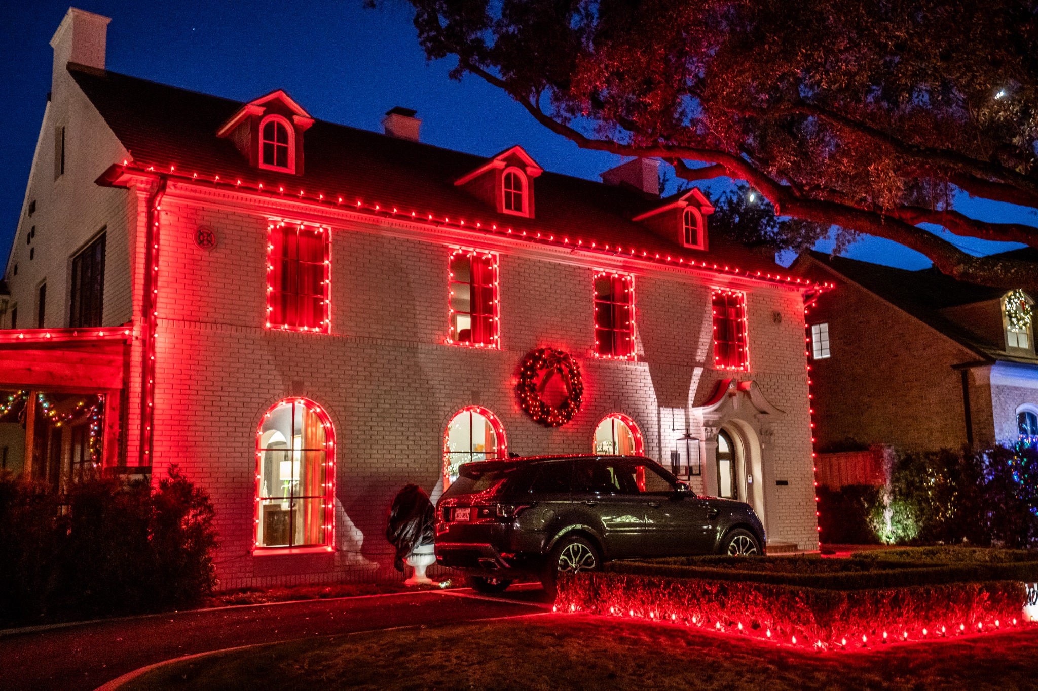 Two-story home outlined in bold red Christmas lights with red landscape accents
