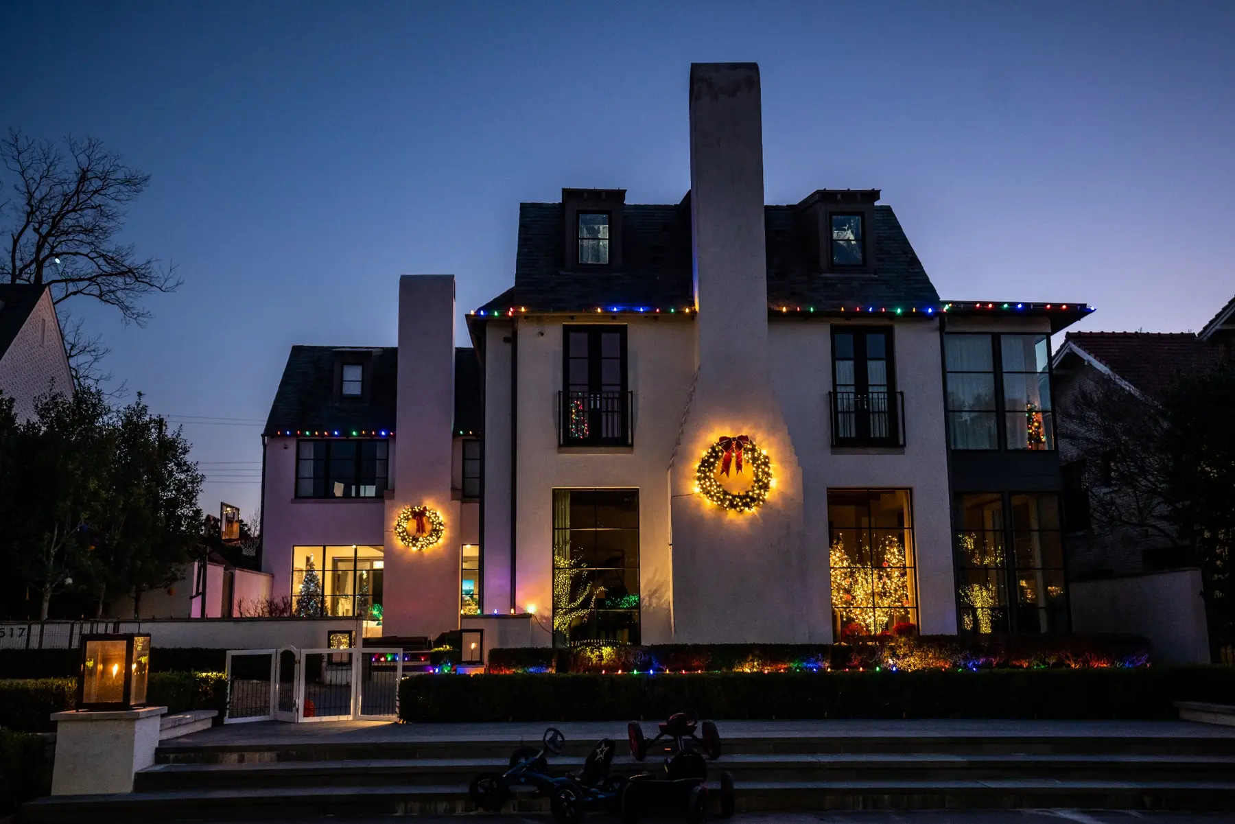Tall two-story home with multicolor roofline accents, lit wreaths and warm white landscape lighting