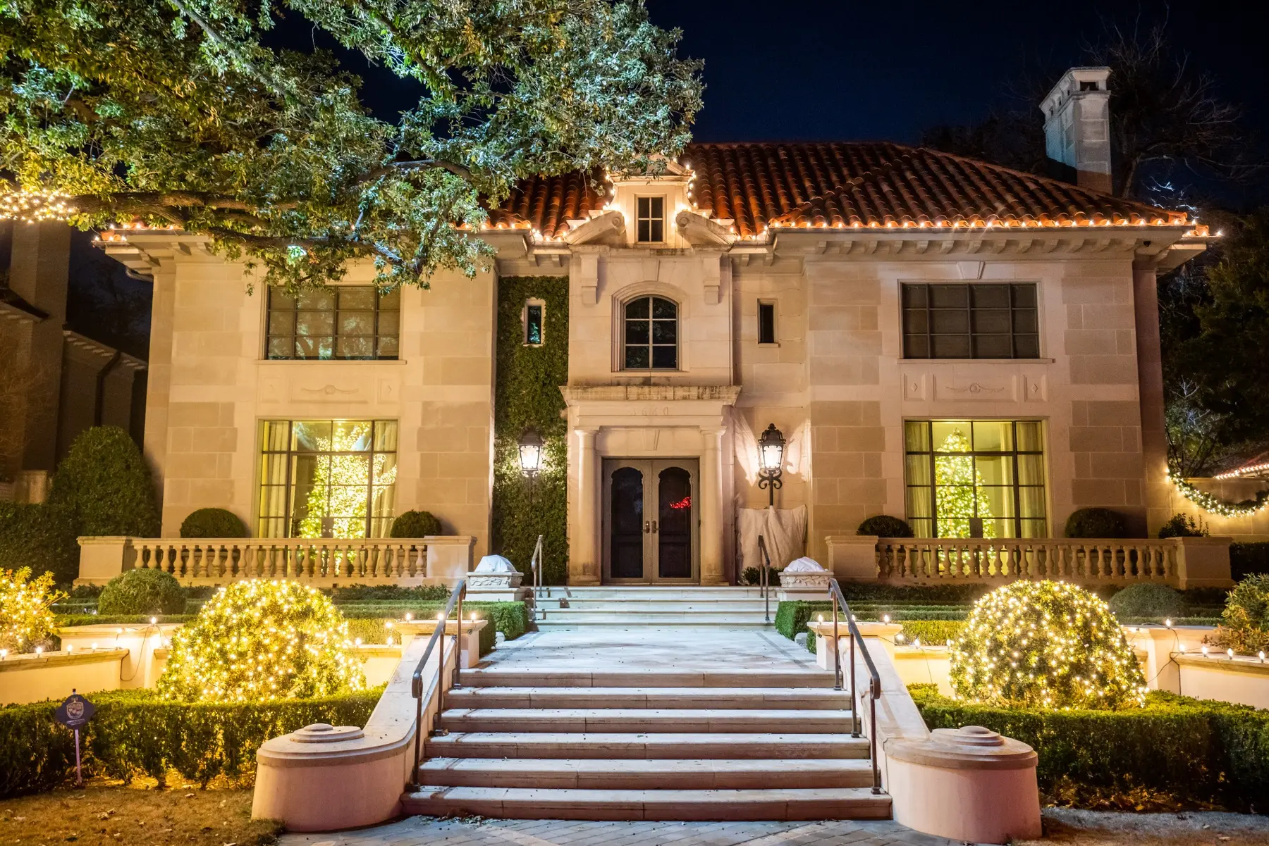 Outdoor holiday lighting across a large residence with trees landscape beds and pathway lighting