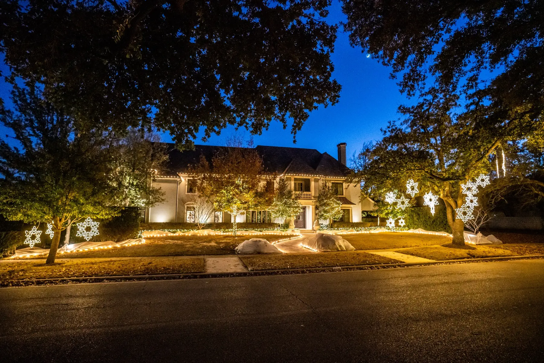 Warm white tree and landscape lighting with illuminated snowflake accents across a large residence