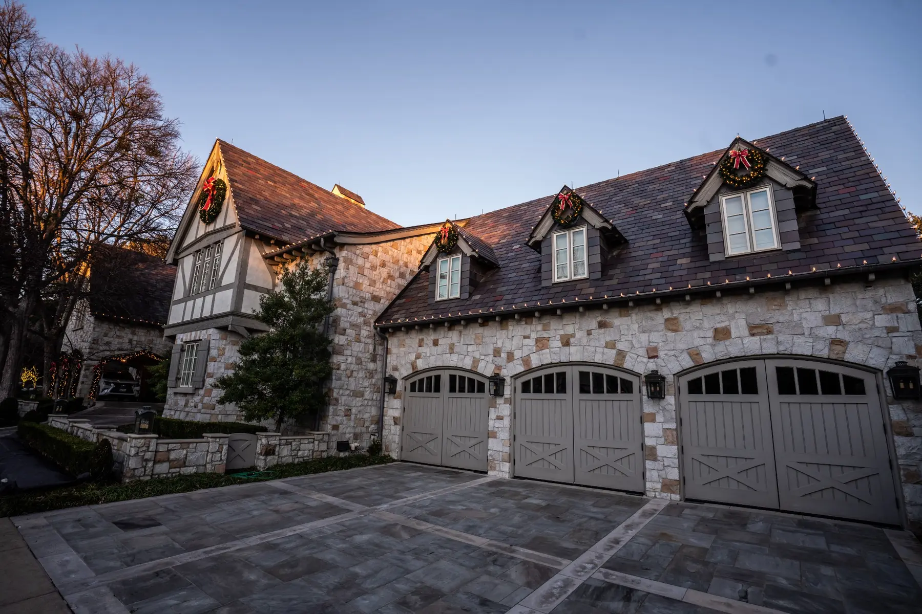 Residential garage accented with holiday wreaths and roofline greenery at dusk